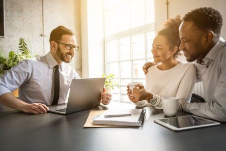 Three people gathered around a table with a laptop, focused on understanding life insurance basics.
