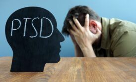 a man with head in hands on a desk inscribed 'PTSD', illustrating the understanding trauma and its impact