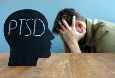 a man with head in hands on a desk inscribed 'PTSD', illustrating the understanding trauma and its impact