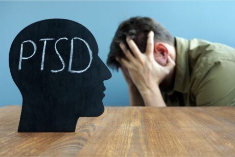 a man with head in hands on a desk inscribed 'PTSD', illustrating the understanding trauma and its impact