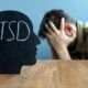 a man with head in hands on a desk inscribed 'PTSD', illustrating the understanding trauma and its impact