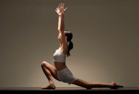 a woman in a white top is engaged in a yoga pose for her hatha yoga online training class