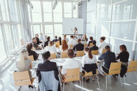 a diverse group of people attentively seated in chairs, facing a large screen displaying engaging content