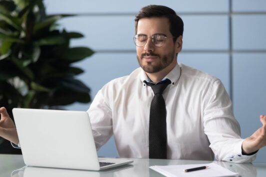 a man dressed in a shirt and tie sits at a desk, hands open, engaged with a laptop, reflecting the concept of peaceful chaos
