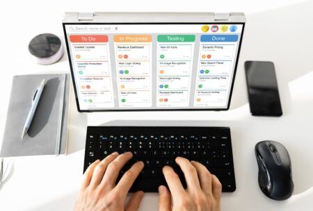 a person types on a laptop displaying a calendar, focusing on scrum and kanban project management methods