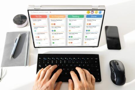 a person types on a laptop displaying a calendar, focusing on scrum and kanban project management methods