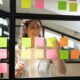 a woman observes a window filled with sticky notes, illustrating her involvement in a scrum master course