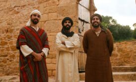three men in traditional clothing stand before a stone building, showcasing how to learn moroccan arabic