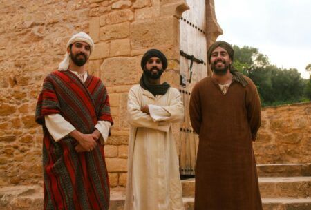 three men in traditional clothing stand before a stone building, showcasing how to learn moroccan arabic