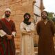 three men in traditional clothing stand before a stone building, showcasing how to learn moroccan arabic
