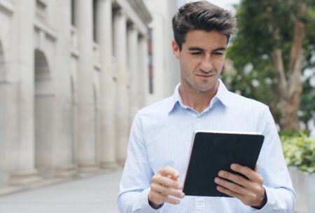 a man in a blue shirt holds a tablet, likely studying for an ACCA course