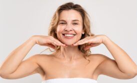 a woman in a towel holds her hands to her face, symbolizing healthy aging and self-care