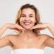a woman in a towel holds her hands to her face, symbolizing healthy aging and self-care