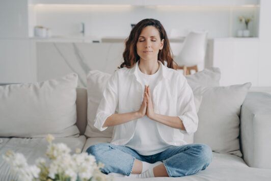 a woman sitting cross-legged on a couch, meditating to promote how to change your mindset
