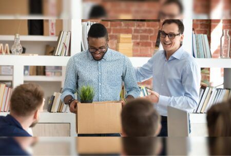 two men in an office hold a box, likely related to HR onboarding materials