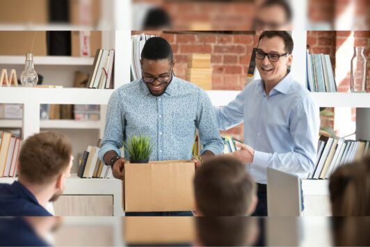 two men in an office hold a box, likely related to HR onboarding materials